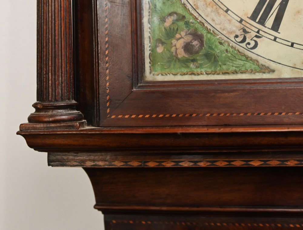 A Georgian mahogany longcase clock featuring a swan-neck pediment with three brass finials, a painted dial with Roman numerals, and a flame mahogany door. View XII