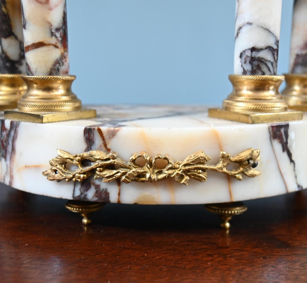 A late nineteenth-century French clock garniture set featuring a central portico clock in purple-veined white marble with gilt bronze mounts, flanked by two matching two-light candelabras. View II