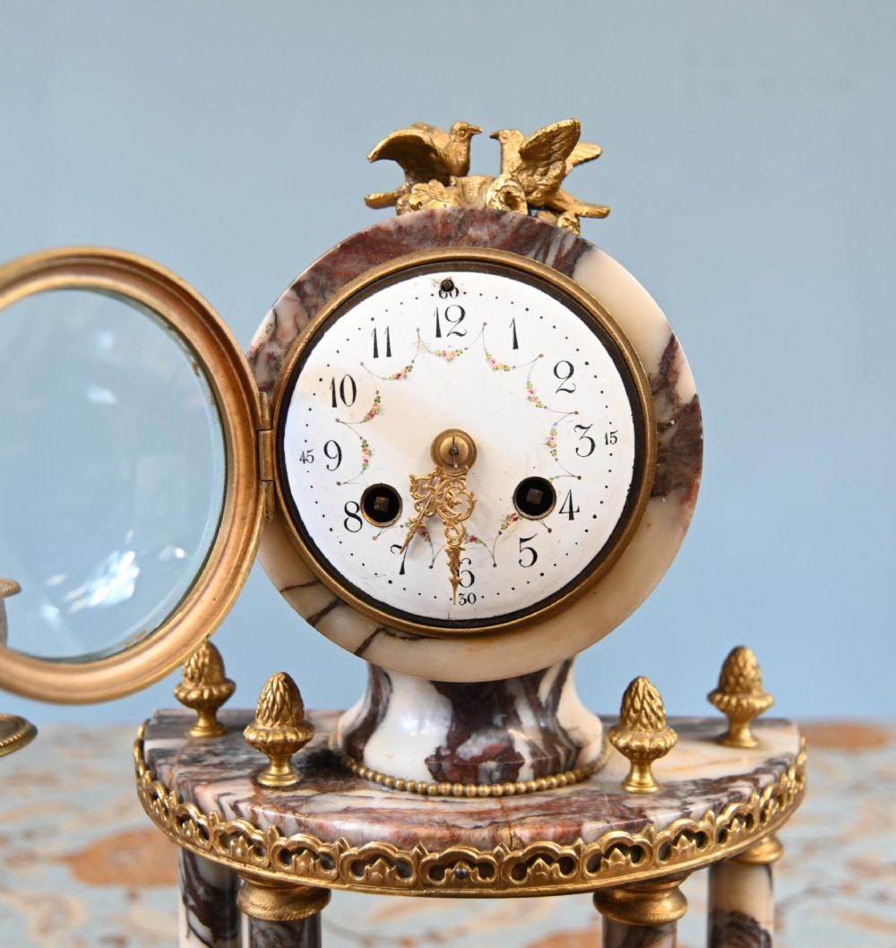 A late nineteenth-century French clock garniture set featuring a central portico clock in purple-veined white marble with gilt bronze mounts, flanked by two matching two-light candelabras. View IV