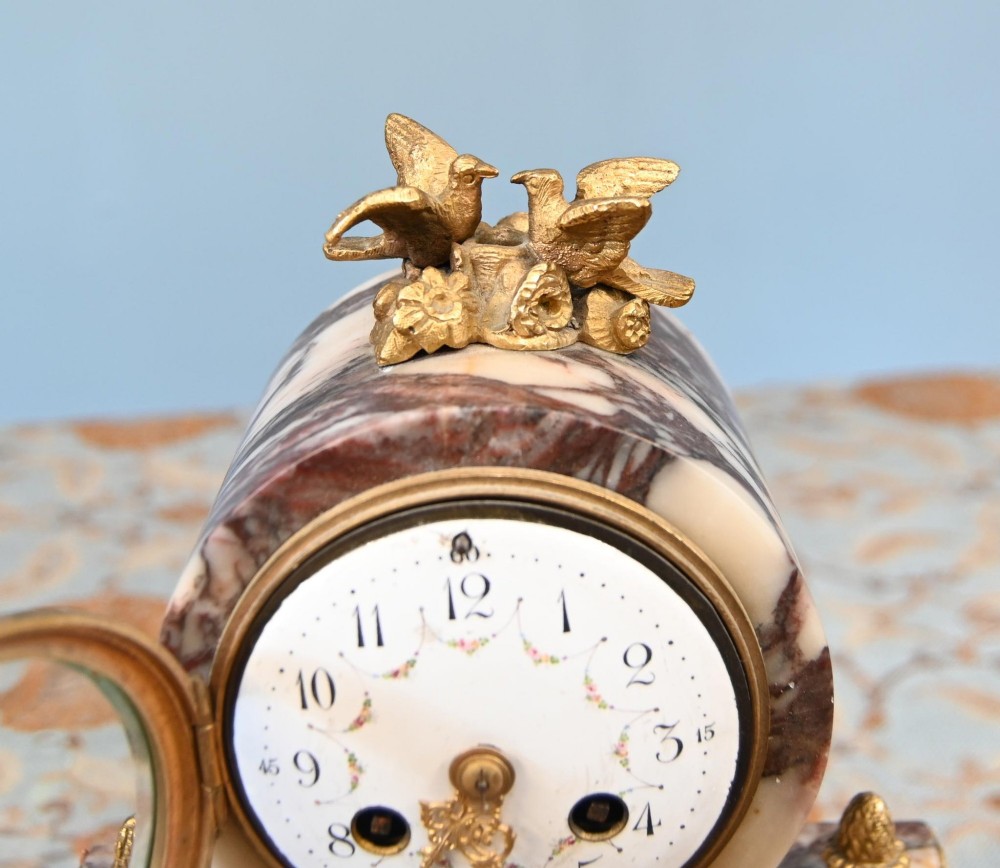 A late nineteenth-century French clock garniture set featuring a central portico clock in purple-veined white marble with gilt bronze mounts, flanked by two matching two-light candelabras. View V