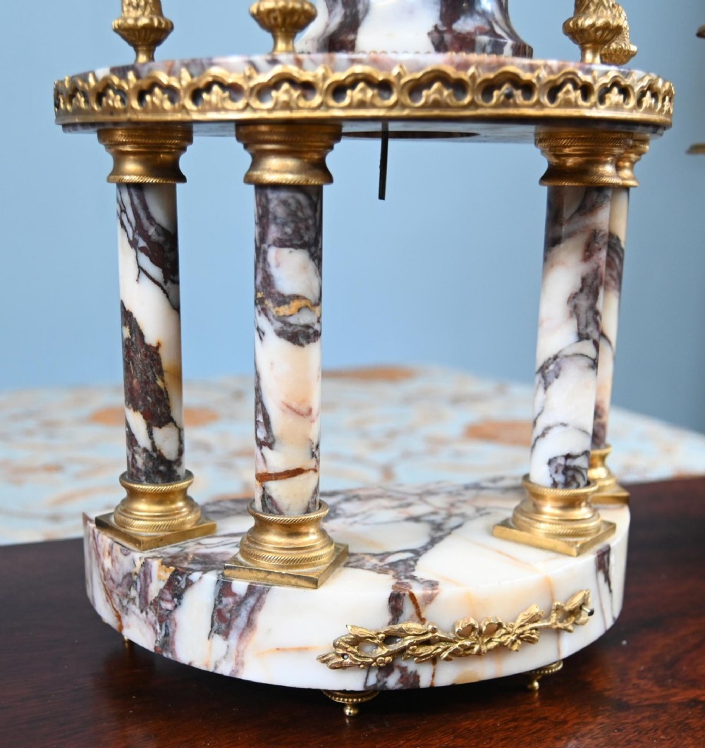 A late nineteenth-century French clock garniture set featuring a central portico clock in purple-veined white marble with gilt bronze mounts, flanked by two matching two-light candelabras. View VIII