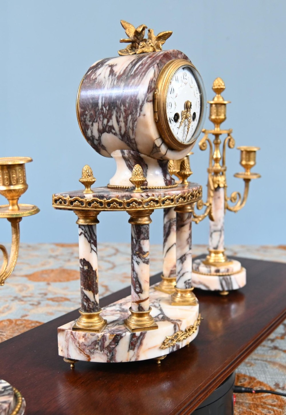 A late nineteenth-century French clock garniture set featuring a central portico clock in purple-veined white marble with gilt bronze mounts, flanked by two matching two-light candelabras. View IX