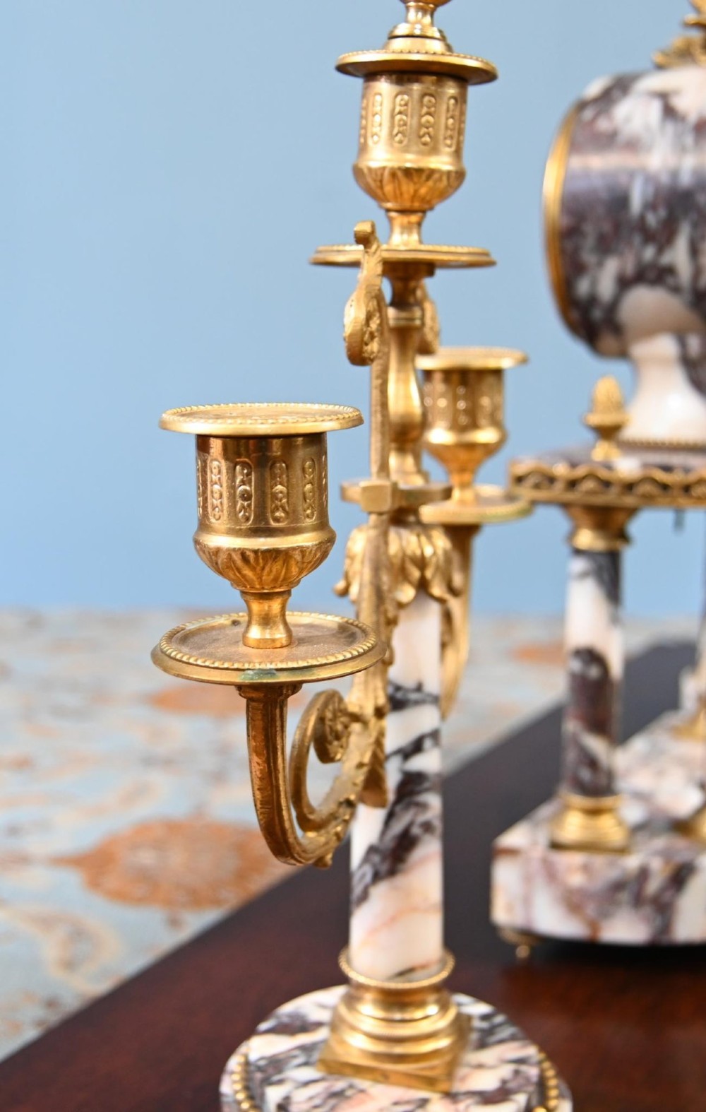 A late nineteenth-century French clock garniture set featuring a central portico clock in purple-veined white marble with gilt bronze mounts, flanked by two matching two-light candelabras. View X