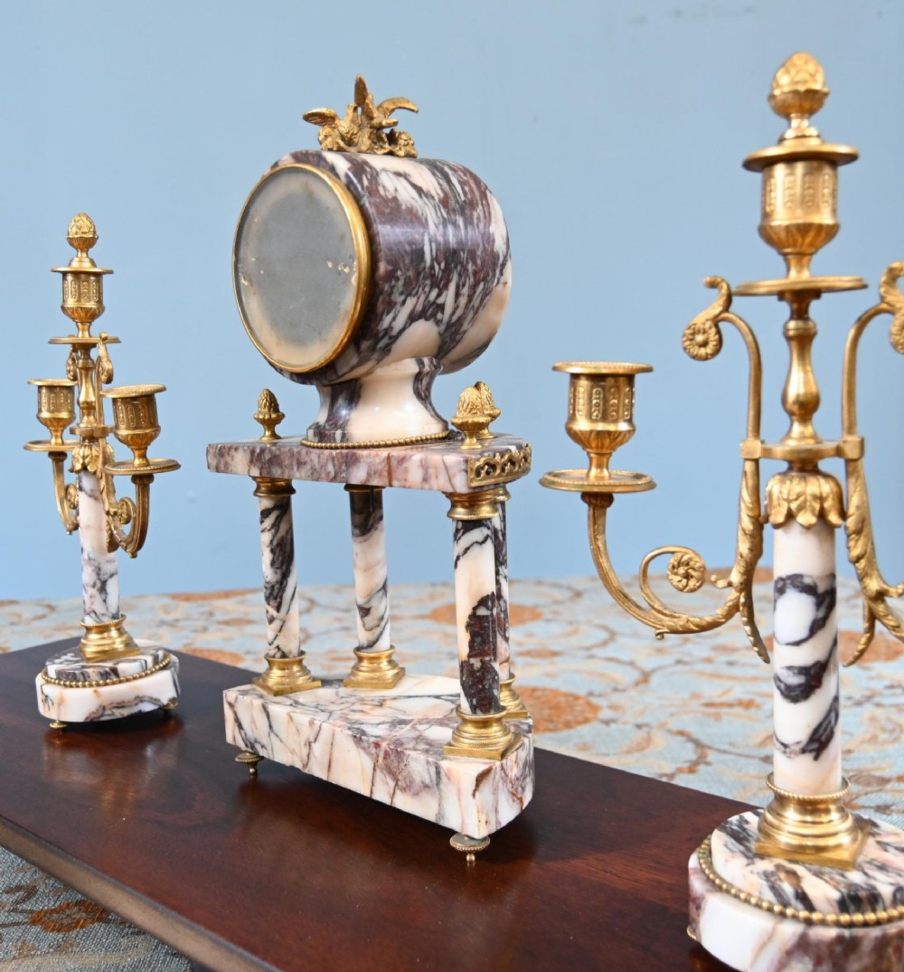 A late nineteenth-century French clock garniture set featuring a central portico clock in purple-veined white marble with gilt bronze mounts, flanked by two matching two-light candelabras. View XI