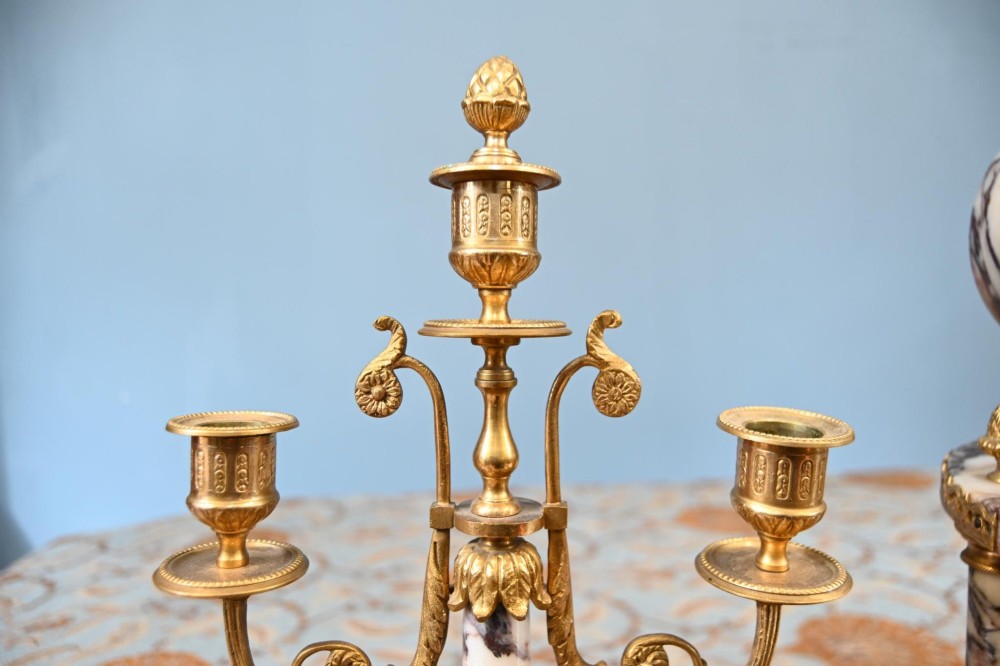 A late nineteenth-century French clock garniture set featuring a central portico clock in purple-veined white marble with gilt bronze mounts, flanked by two matching two-light candelabras. View XIII