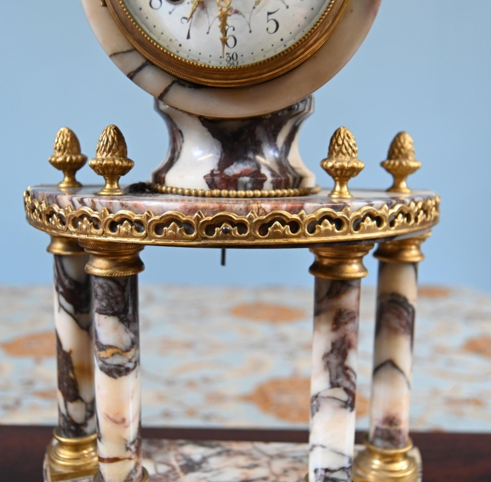 A late nineteenth-century French clock garniture set featuring a central portico clock in purple-veined white marble with gilt bronze mounts, flanked by two matching two-light candelabras. View XIV