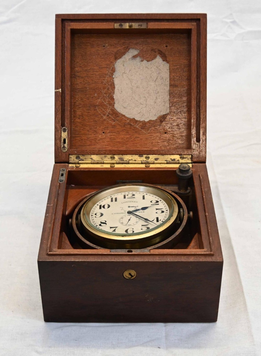 A 1920s Longines marine chronometer clock with a white dial set in a brass gimbal mechanism inside an open mahogany box.