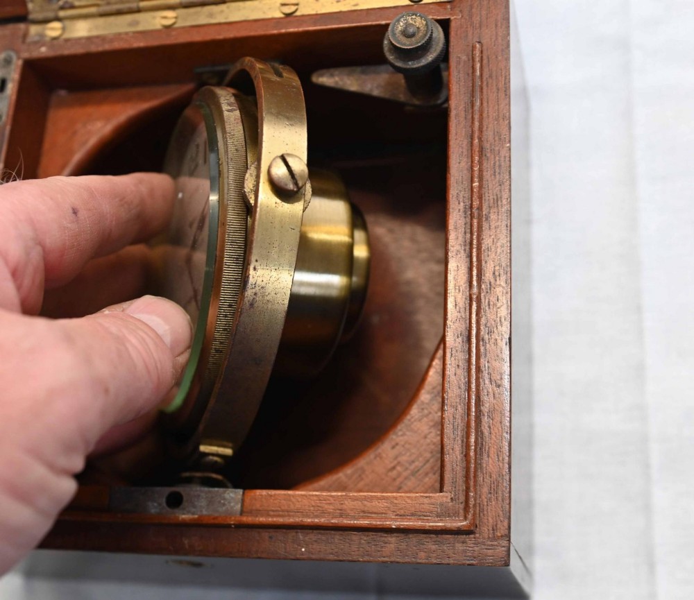 A 1920s Longines marine chronometer clock with a white dial set in a brass gimbal mechanism inside an open mahogany box. View III