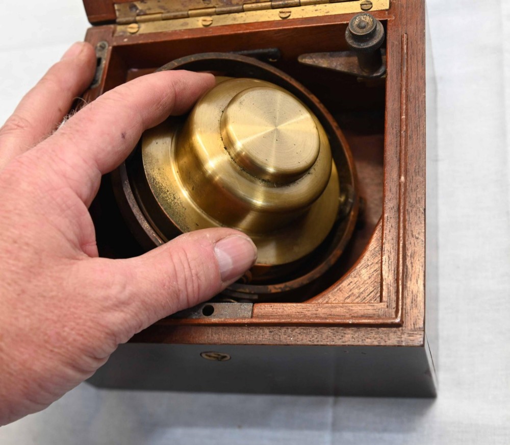 A 1920s Longines marine chronometer clock with a white dial set in a brass gimbal mechanism inside an open mahogany box. View V