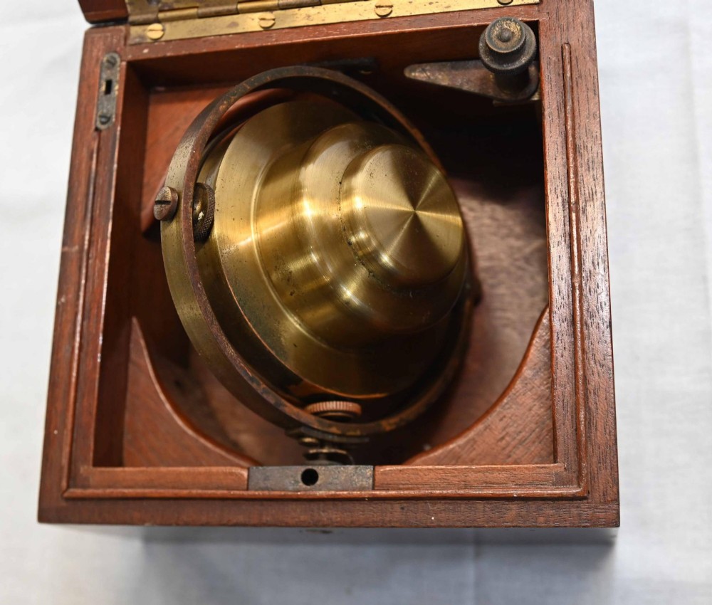 A 1920s Longines marine chronometer clock with a white dial set in a brass gimbal mechanism inside an open mahogany box. View VI