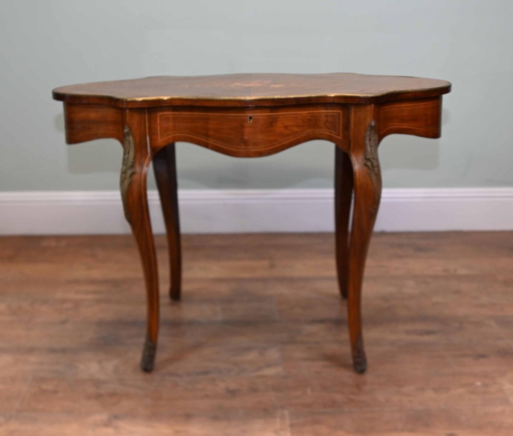A French Louis XV style writing desk crafted from brown wood with a serpentine top, floral marquetry inlay, cabriole legs, and brass mounts. View V