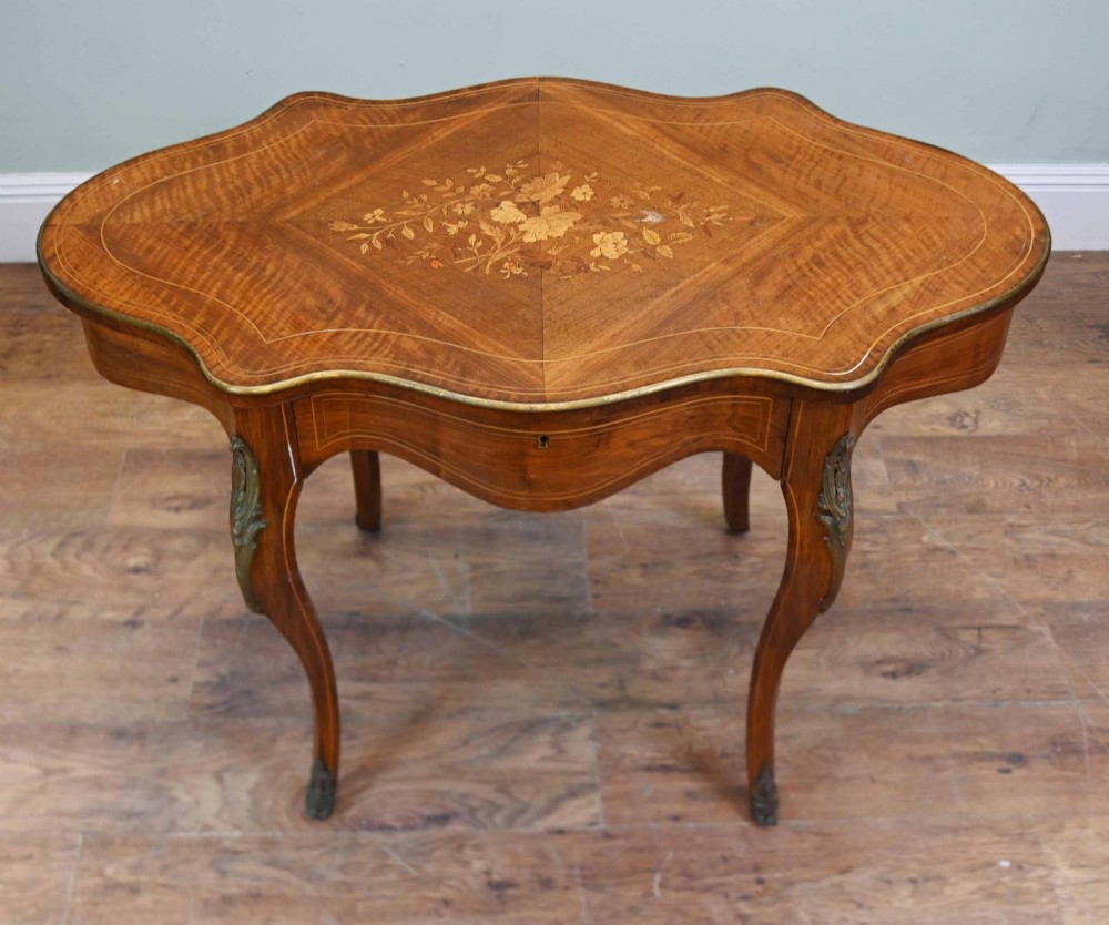 A French Louis XV style writing desk crafted from brown wood with a serpentine top, floral marquetry inlay, cabriole legs, and brass mounts. View VI