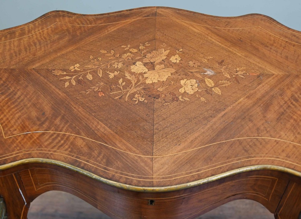 A French Louis XV style writing desk crafted from brown wood with a serpentine top, floral marquetry inlay, cabriole legs, and brass mounts. View VII