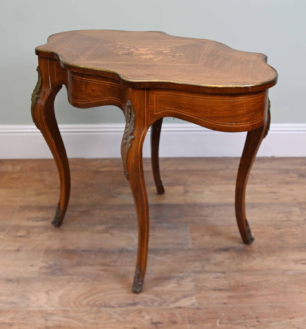 A French Louis XV style writing desk crafted from brown wood with a serpentine top, floral marquetry inlay, cabriole legs, and brass mounts. View X