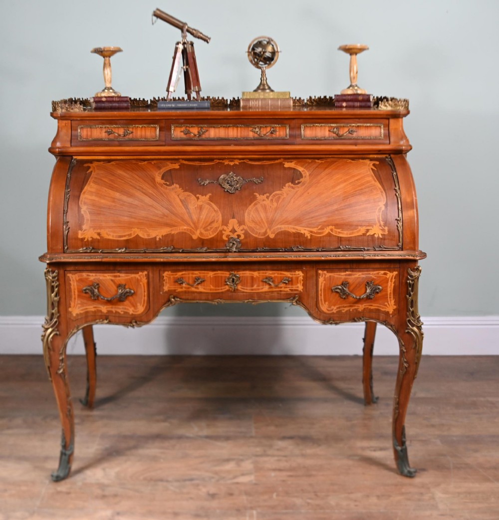 An antique French roll-top bureau featuring wood marquetry inlay, decorative brass mounts, cabriole legs, and drawers.