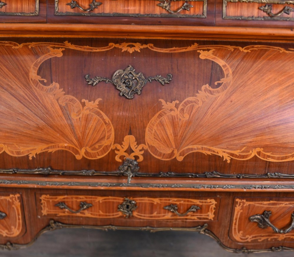 An antique French roll-top bureau featuring wood marquetry inlay, decorative brass mounts, cabriole legs, and drawers. View III