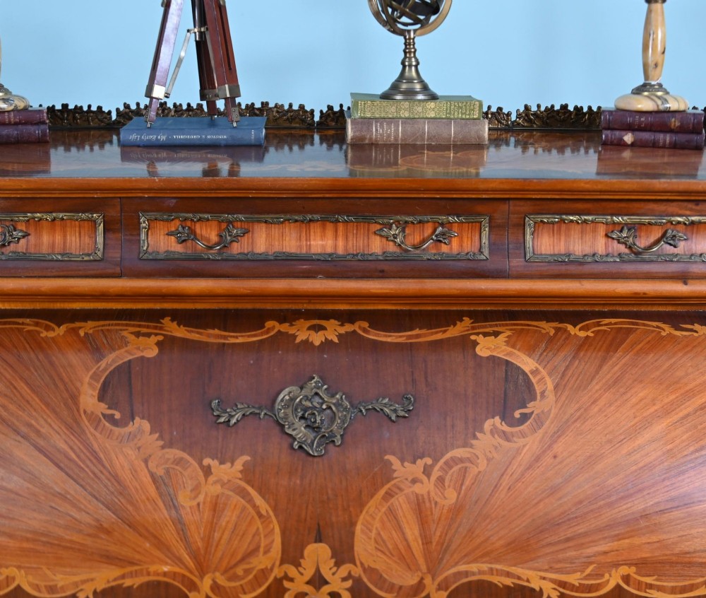 An antique French roll-top bureau featuring wood marquetry inlay, decorative brass mounts, cabriole legs, and drawers. View IV