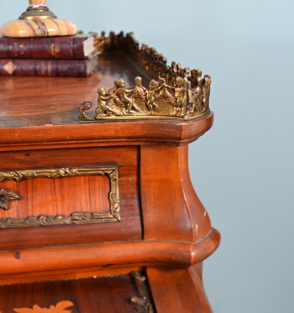 An antique French roll-top bureau featuring wood marquetry inlay, decorative brass mounts, cabriole legs, and drawers. View VII