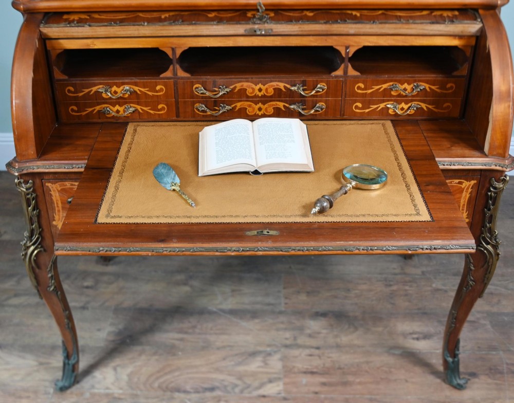 An antique French roll-top bureau featuring wood marquetry inlay, decorative brass mounts, cabriole legs, and drawers. View XI