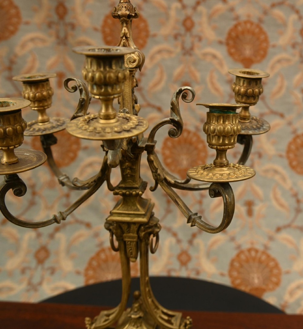 A 19th-century Louis XVI style gilt bronze clock garniture set comprising a central ornate mantel clock flanked by two matching five-light candelabras. View IV