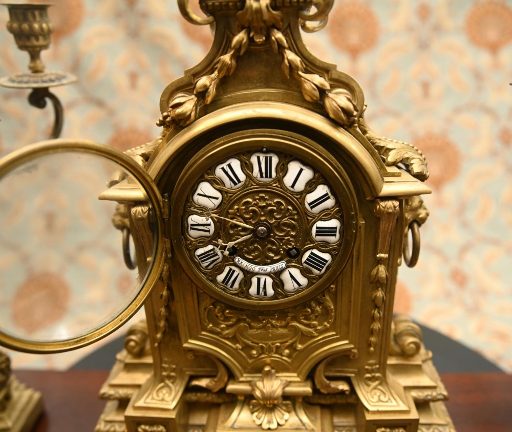 A 19th-century Louis XVI style gilt bronze clock garniture set comprising a central ornate mantel clock flanked by two matching five-light candelabras. View VI