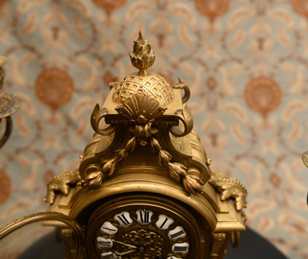 A 19th-century Louis XVI style gilt bronze clock garniture set comprising a central ornate mantel clock flanked by two matching five-light candelabras. View VIII