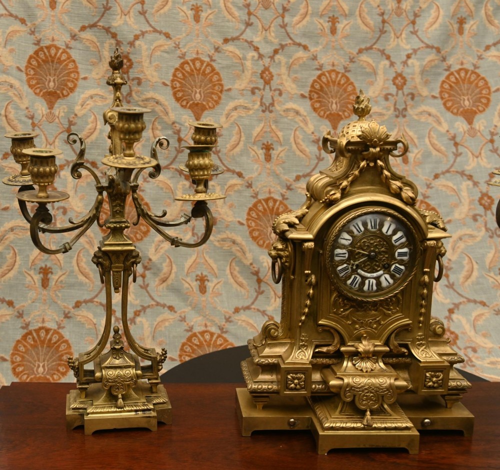 A 19th-century Louis XVI style gilt bronze clock garniture set comprising a central ornate mantel clock flanked by two matching five-light candelabras. View IX