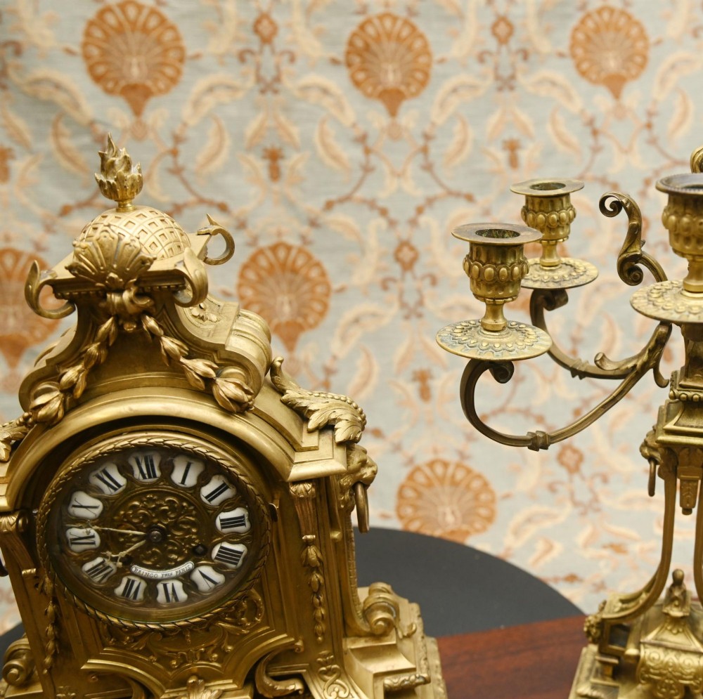 A 19th-century Louis XVI style gilt bronze clock garniture set comprising a central ornate mantel clock flanked by two matching five-light candelabras. View X