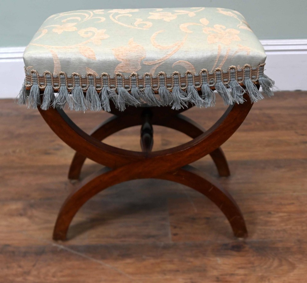 A Regency style mahogany stool featuring curved x-frame legs, a central turned stretcher, and a pale blue patterned damask upholstered seat finished with grey fringe trim. View V
