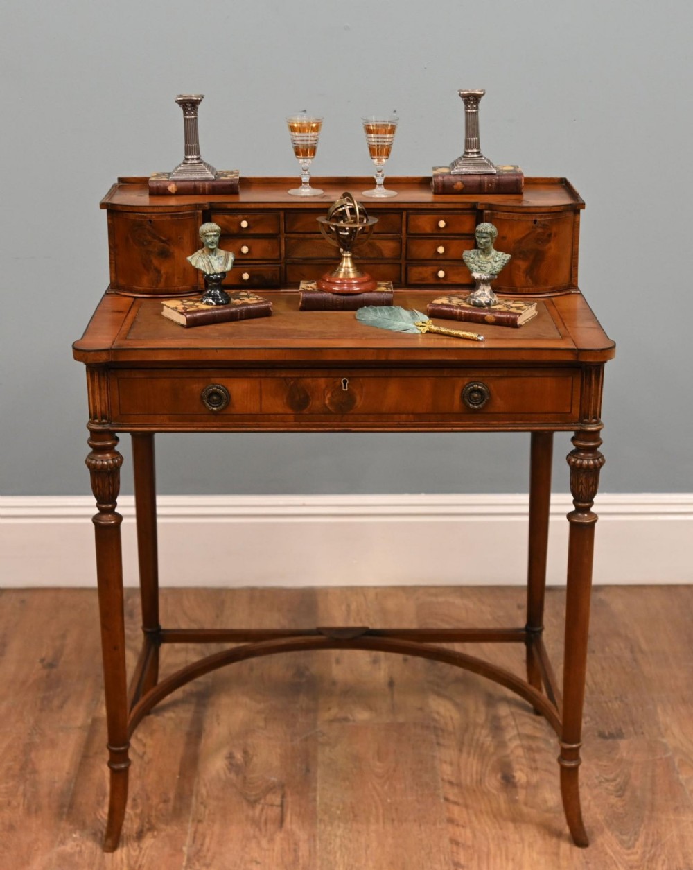 A Regency Revival mahogany ladies writing desk featuring a leather-lined writing surface, elevated drawer superstructure, turned reeded legs, and a curved stretcher.