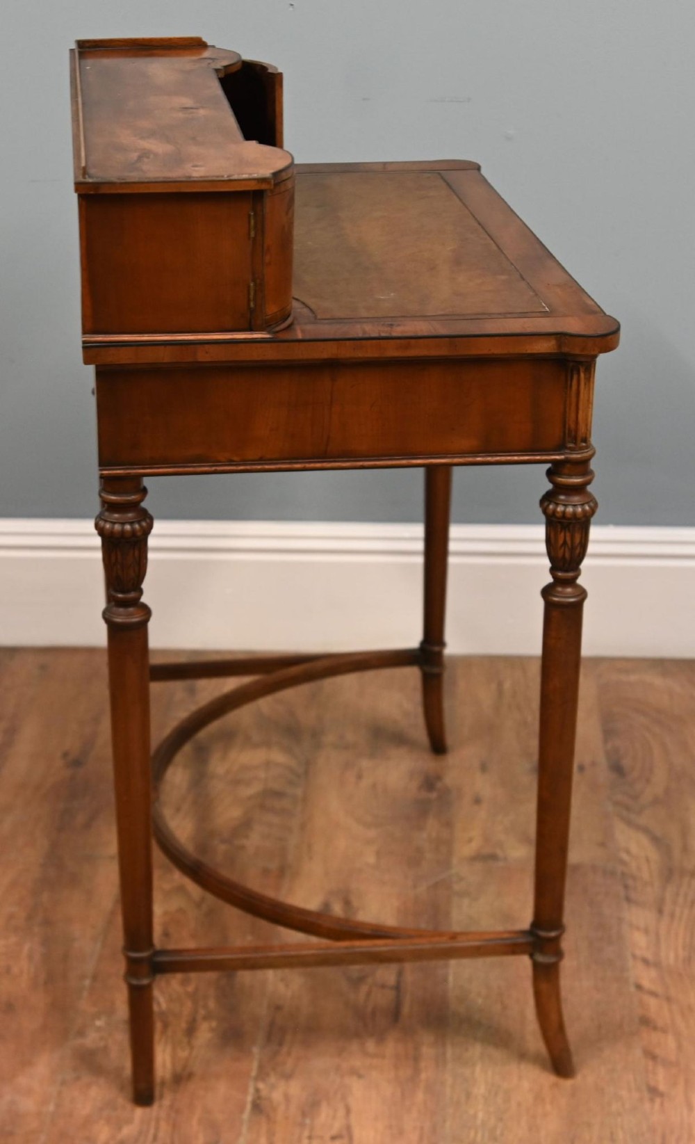 A Regency Revival mahogany ladies writing desk featuring a leather-lined writing surface, elevated drawer superstructure, turned reeded legs, and a curved stretcher. View V
