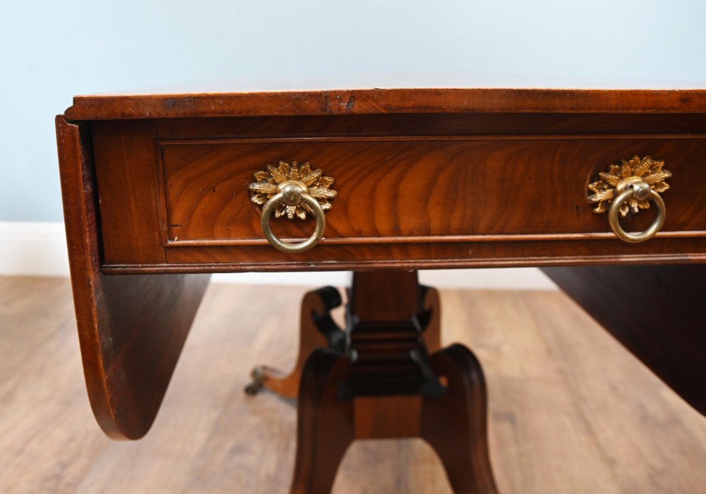 A Regency mahogany drop-leaf table featuring flame veneer panels and a central pedestal supported by four splayed legs with brass claw feet and castors. View II