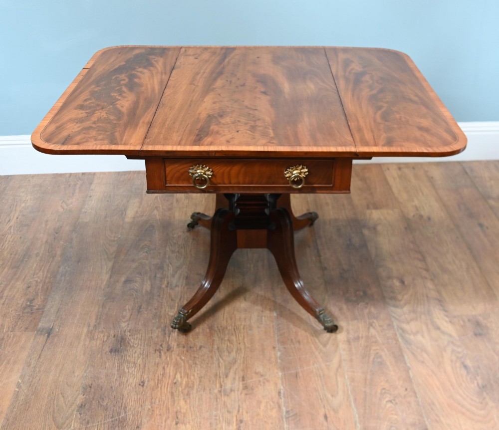 A Regency mahogany drop-leaf table featuring flame veneer panels and a central pedestal supported by four splayed legs with brass claw feet and castors. View III