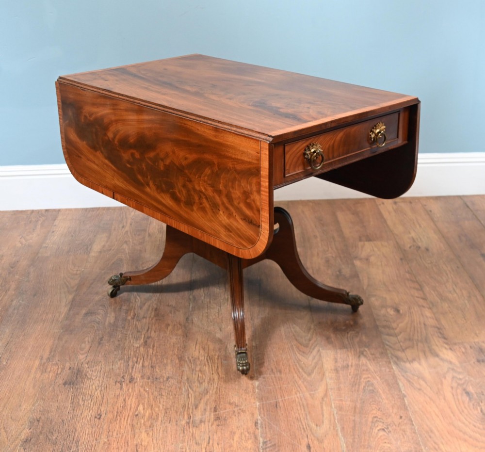 A Regency mahogany drop-leaf table featuring flame veneer panels and a central pedestal supported by four splayed legs with brass claw feet and castors. View IV
