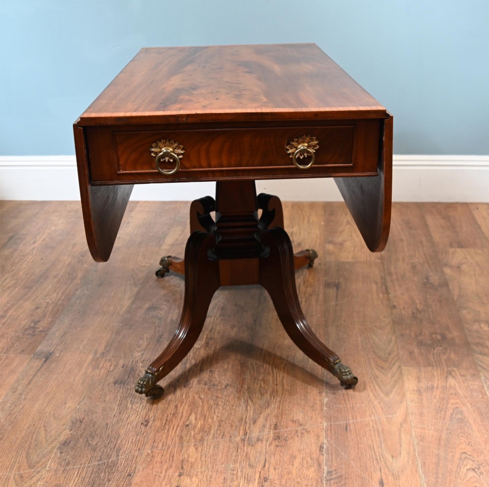 A Regency mahogany drop-leaf table featuring flame veneer panels and a central pedestal supported by four splayed legs with brass claw feet and castors. View V