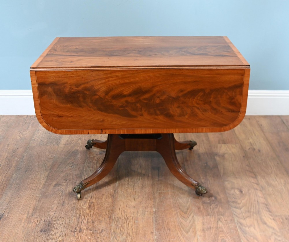 A Regency mahogany drop-leaf table featuring flame veneer panels and a central pedestal supported by four splayed legs with brass claw feet and castors. View VI