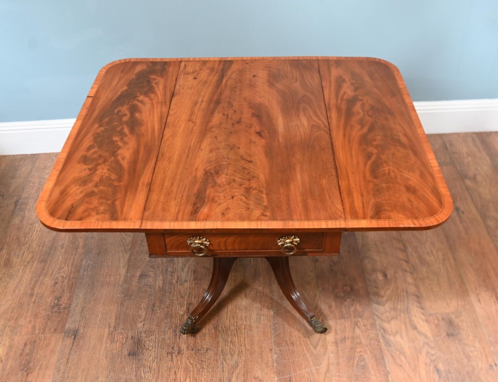 A Regency mahogany drop-leaf table featuring flame veneer panels and a central pedestal supported by four splayed legs with brass claw feet and castors. View VII