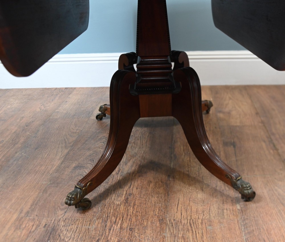A Regency mahogany drop-leaf table featuring flame veneer panels and a central pedestal supported by four splayed legs with brass claw feet and castors. View VIII