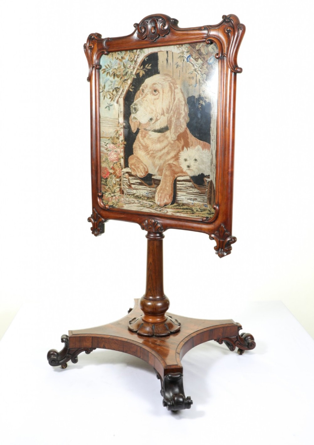 A Victorian carved mahogany fire screen featuring a needlepoint tapestry panel depicting a large hound and a small terrier inside a wooden kennel. View II