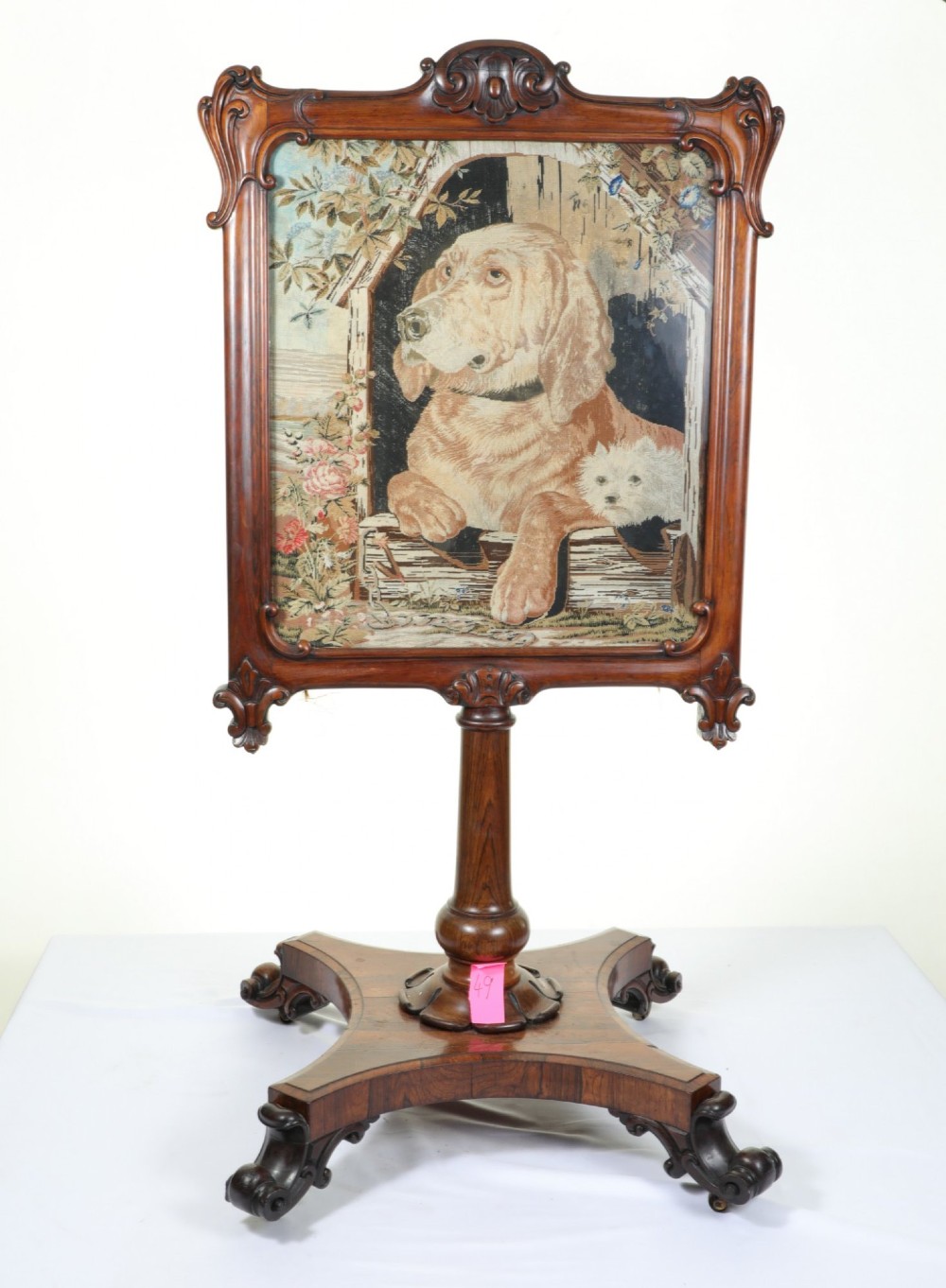 A Victorian carved mahogany fire screen featuring a needlepoint tapestry panel depicting a large hound and a small terrier inside a wooden kennel. View V