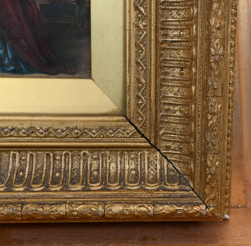 A 19th-century Victorian oil painting depicting figures in historical dress examining a portrait by candlelight, set within a heavily carved gold gilt frame. View V