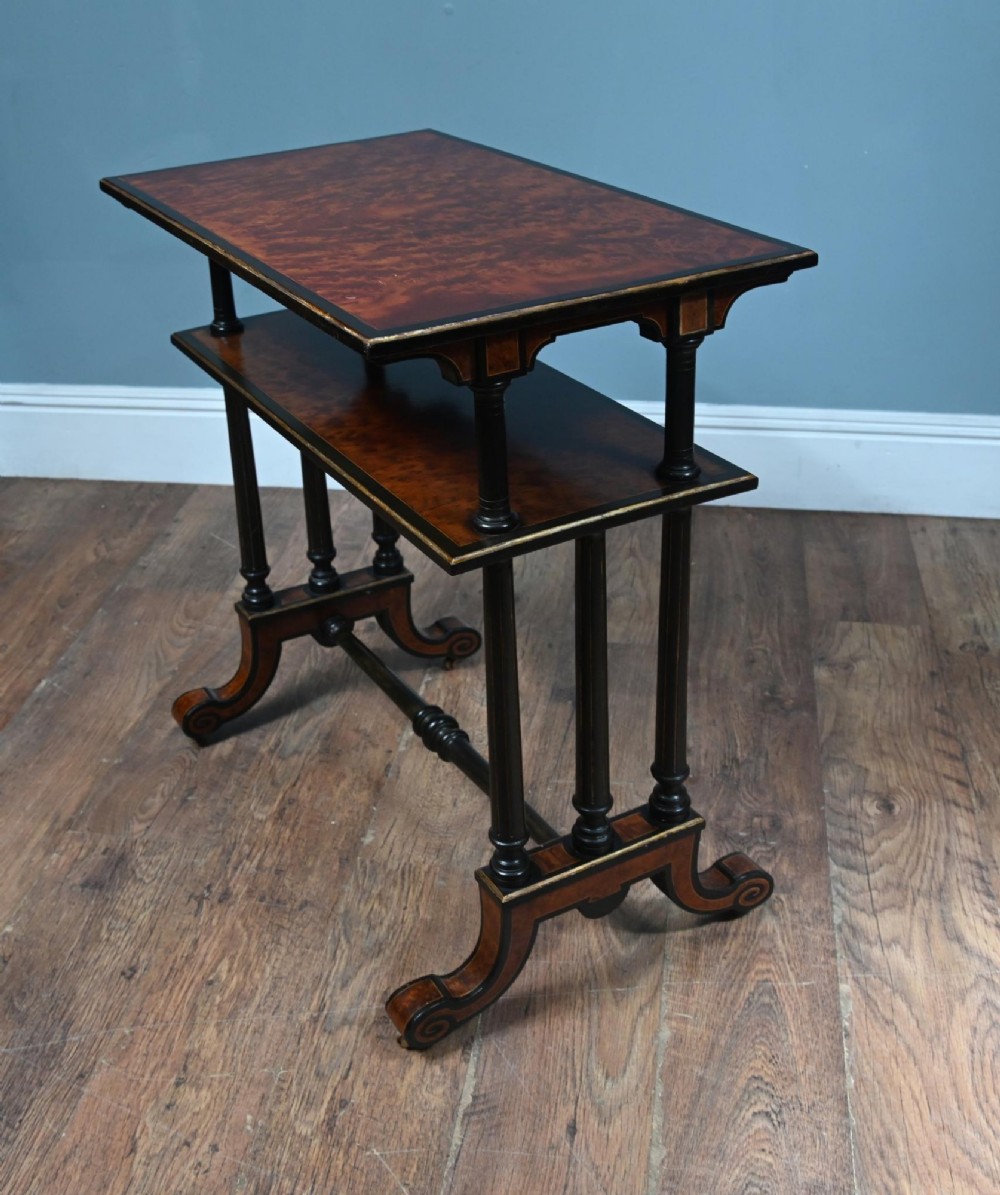 A late Victorian two-tier dumb waiter with warm amboyna wood surfaces, ebonised turned column supports, and splayed legs on castors. View III