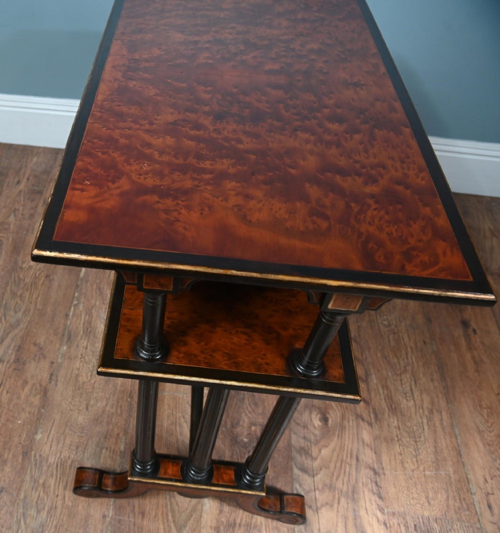 A late Victorian two-tier dumb waiter with warm amboyna wood surfaces, ebonised turned column supports, and splayed legs on castors. View VI