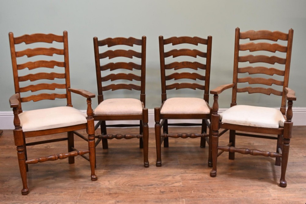 A set of four Edwardian oak ladderback dining chairs featuring two armchairs and two side chairs with turned legs and cream fabric seats.
