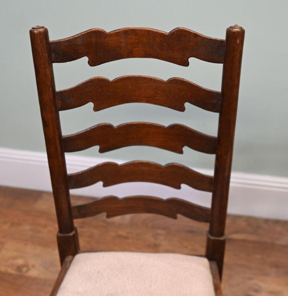 A set of four Edwardian oak ladderback dining chairs featuring two armchairs and two side chairs with turned legs and cream fabric seats. View VI