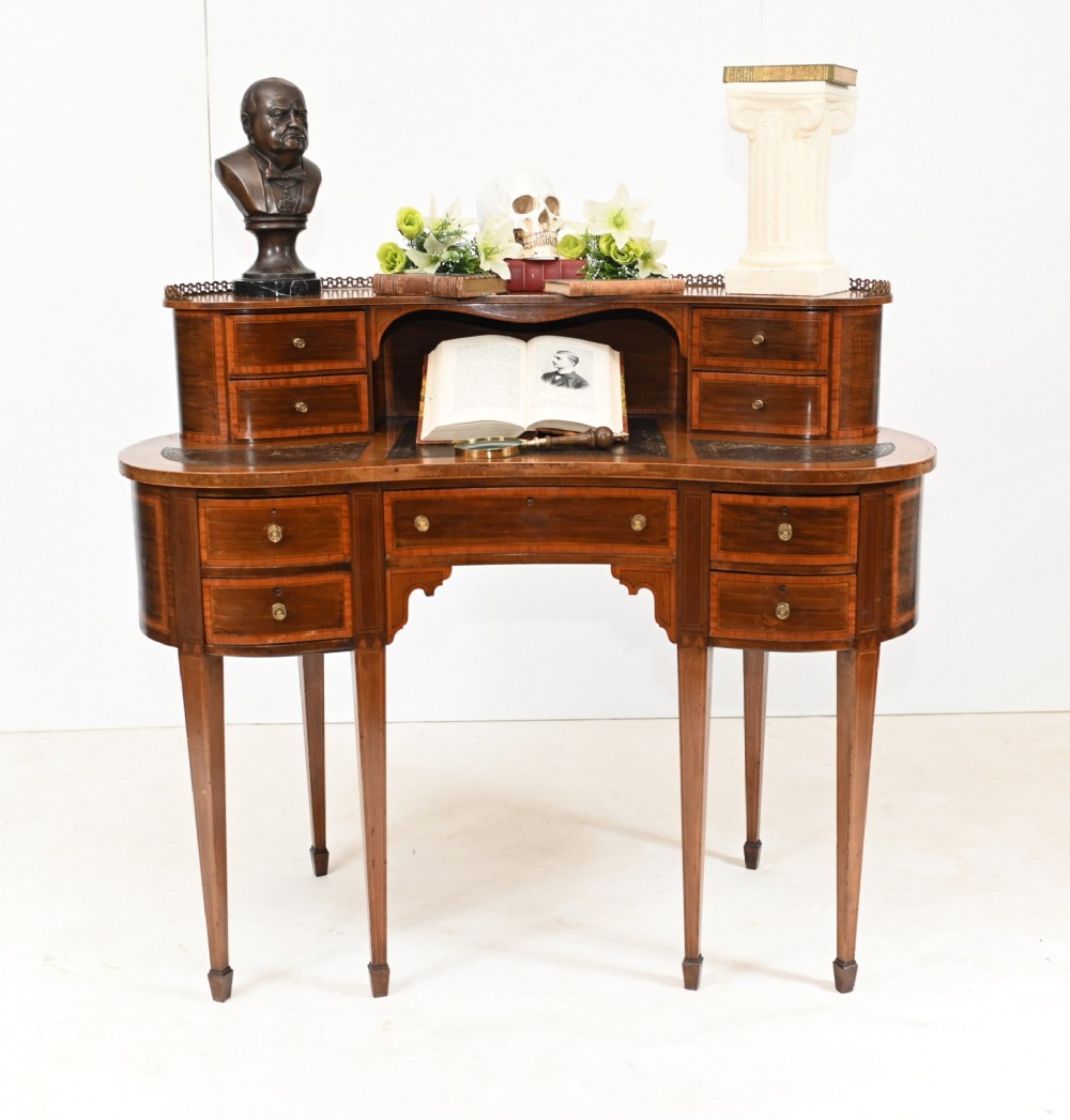 An Edwardian inlaid mahogany kidney-shaped writing desk featuring a raised superstructure with drawers, a central alcove, a leather writing surface, and tapered square legs.