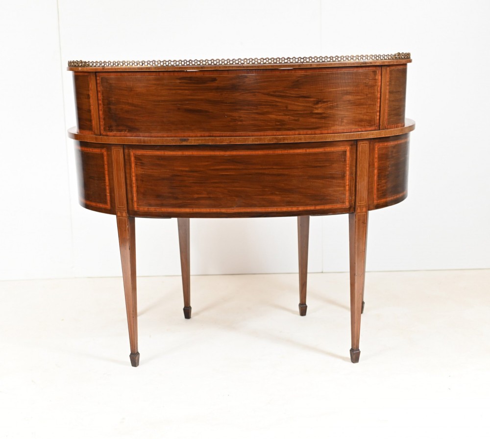 An Edwardian inlaid mahogany kidney-shaped writing desk featuring a raised superstructure with drawers, a central alcove, a leather writing surface, and tapered square legs. View IX