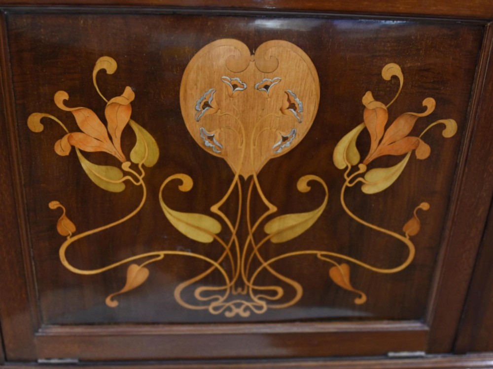 An Edwardian Art Nouveau dark mahogany drinks cabinet featuring stylised botanical marquetry inlays, twin glazed side doors, two lower drawers, and slender splayed legs. View V