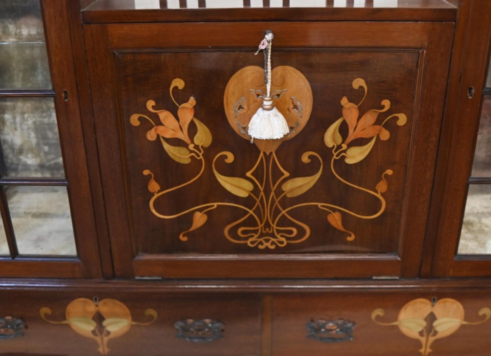 An Edwardian Art Nouveau dark mahogany drinks cabinet featuring stylised botanical marquetry inlays, twin glazed side doors, two lower drawers, and slender splayed legs. View VIII