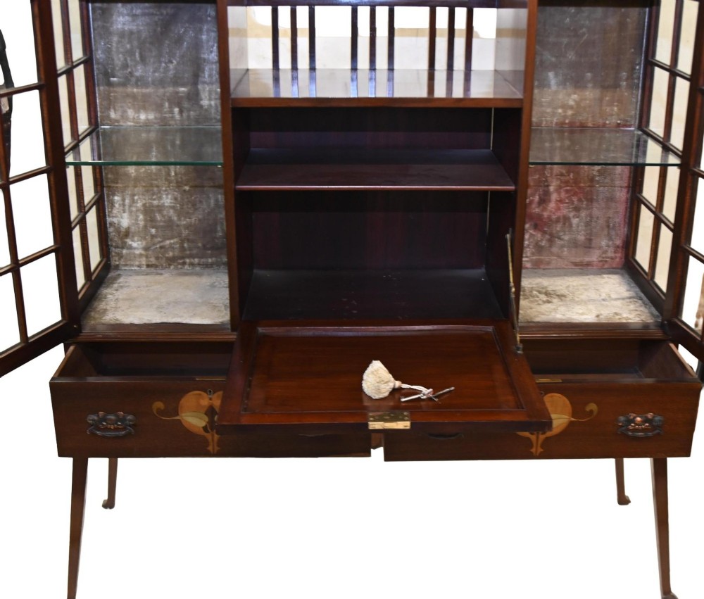 An Edwardian Art Nouveau dark mahogany drinks cabinet featuring stylised botanical marquetry inlays, twin glazed side doors, two lower drawers, and slender splayed legs. View XII